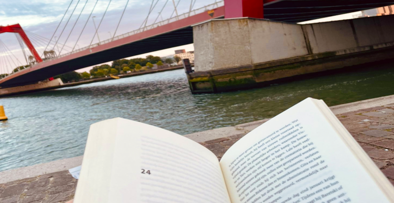 Op de voorgrond een opengeslagen boek en op de achtergrond de Willemsbrug in Rotterdam