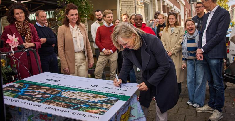 Wethouder Zeegers zet haar handtekening onder het partnerschap met stichting Samen Tegen Voedselverspilling. Een groep mensen, waaronder gedeputeerde Van Leeuwen van de Provincie Zuid-Holland kijken toe.