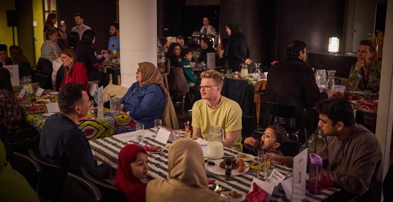 Groep mensen zit samen aan lange tafel te eten.