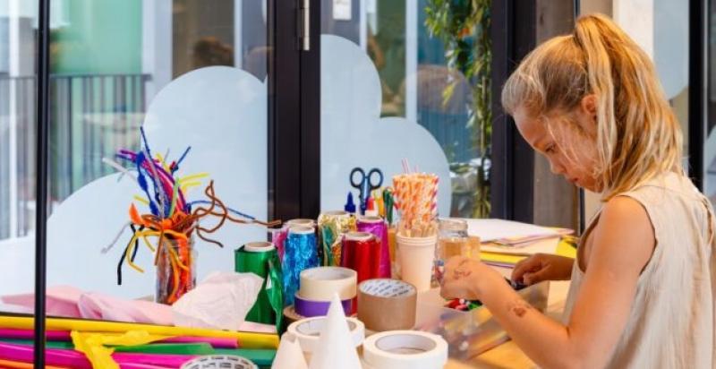 Een meisje staat aan een tafel vol met kleurrijke knutselmaterialen