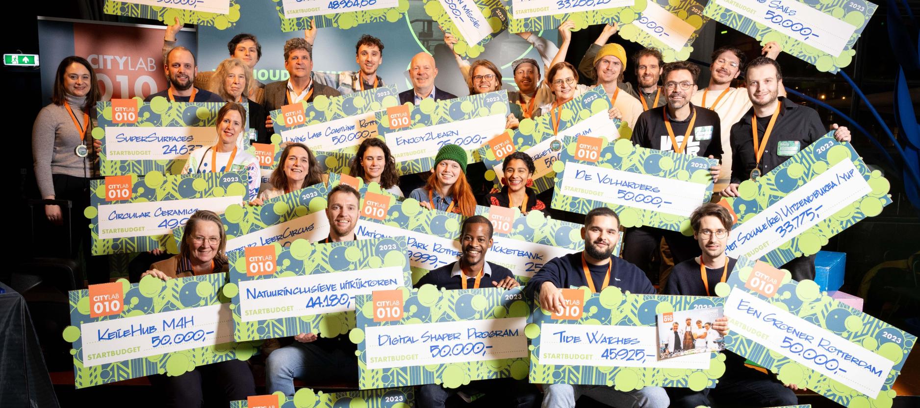 groepsfoto van lachende Rotterdamse initiatiefnemers met cheque in de hand, met daarop het startbedrag voor hun initiatief
