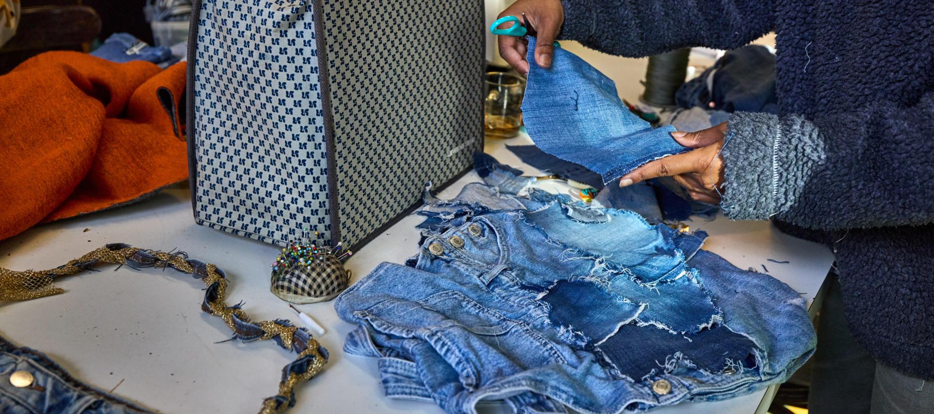 Vrouw is op een tafel bezig met het naaien van spijkerstof