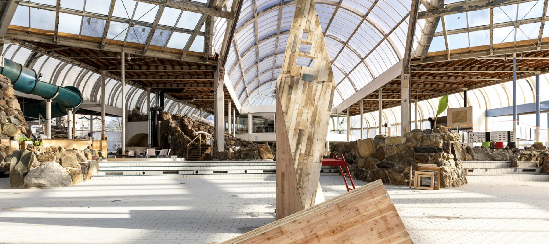 Bouwwerk gemaakt is van kruislaaghout van tweedehands pallets in het oude lege zwembad Tropicana, onder koepelglas dak. 