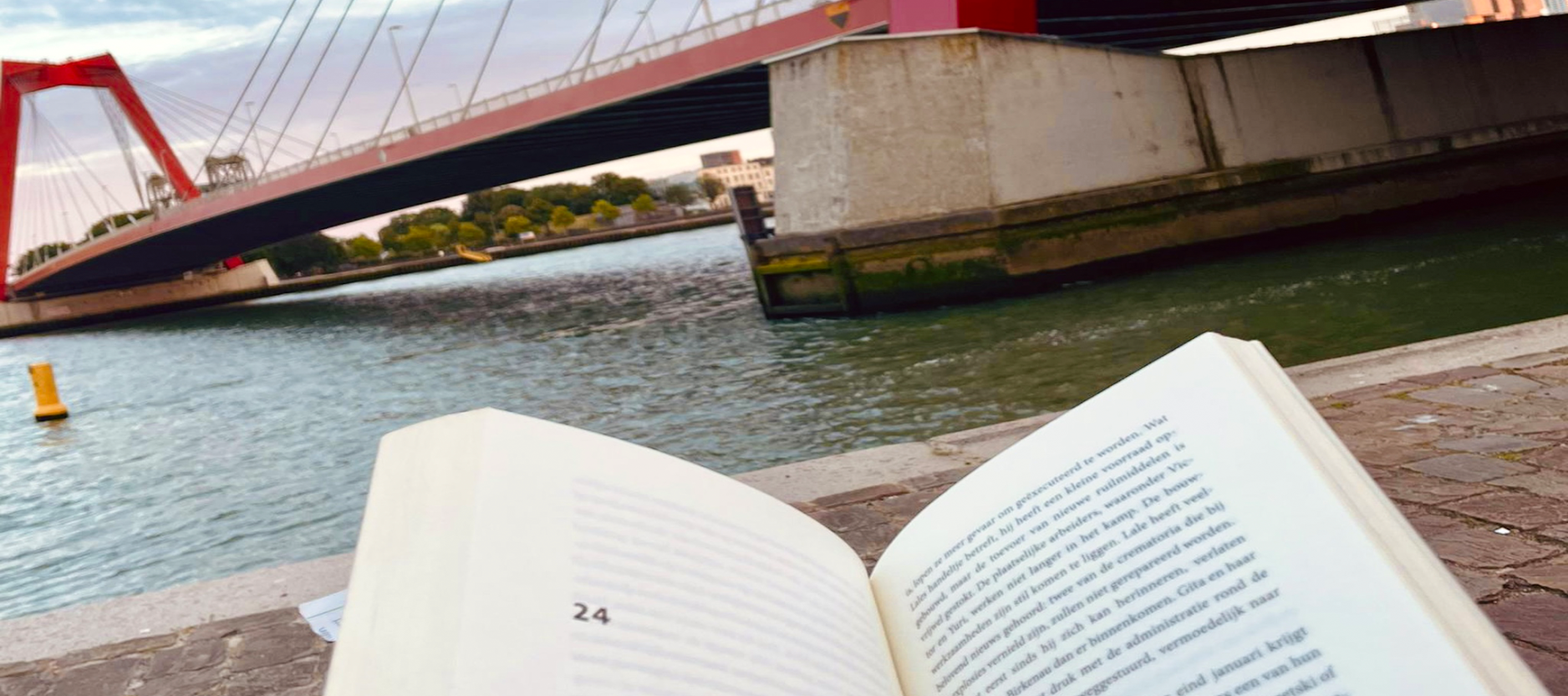 Op de voorgrond een opengeslagen boek en op de achtergrond de Willemsbrug in Rotterdam