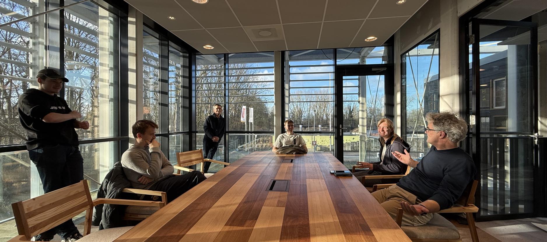 Mensen zitten om een houten vergadertafel in circulair centrum De HER