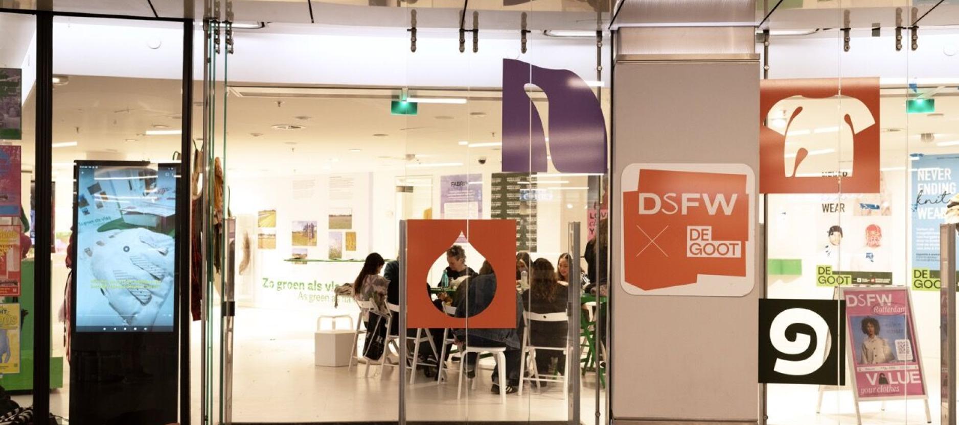 Door een winkelruit is een groepje mensen zichtbaar die aan een tafel zitten.