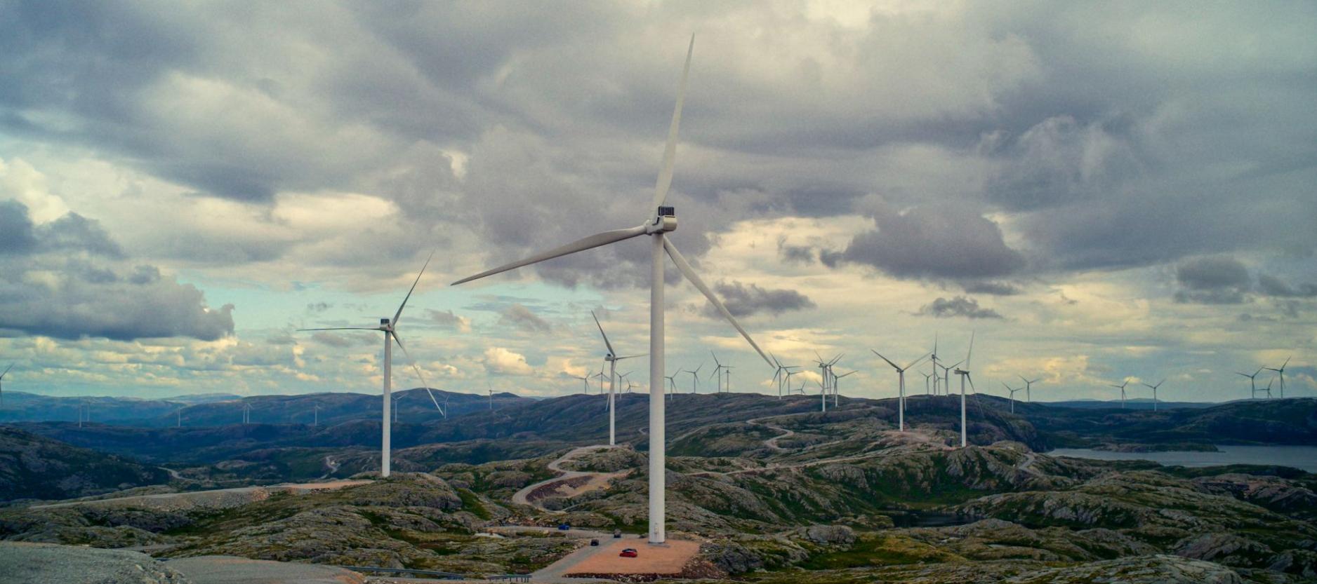 Windturbines verspreid over een uitgestrekt, rotsachtig heuvellandschap onder een zwaarbewolkte lucht.