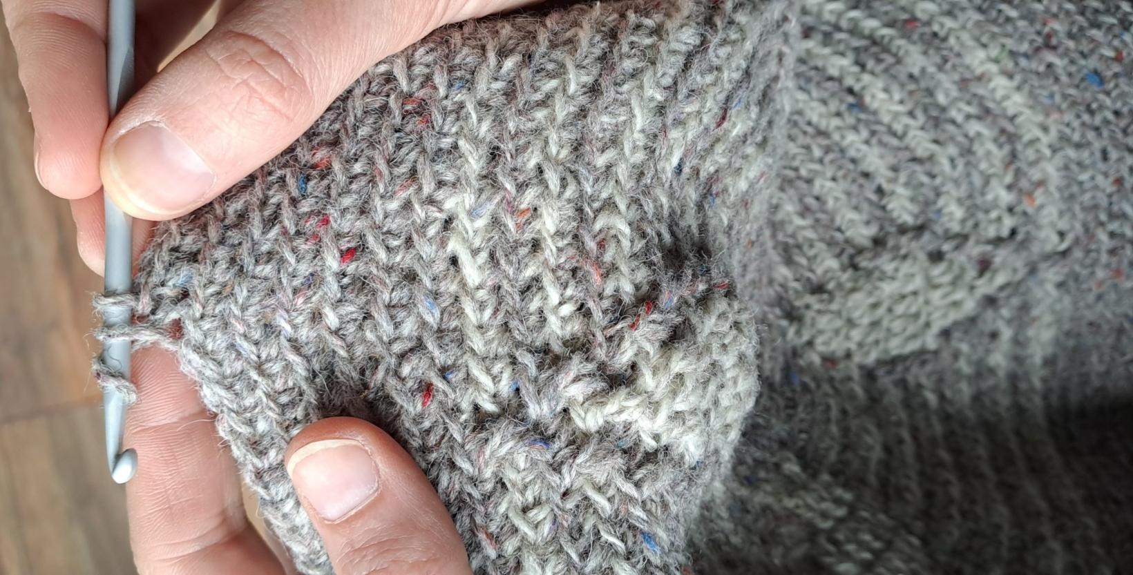 close-up van handen, die met grijze haak een stuk grijze wol haken