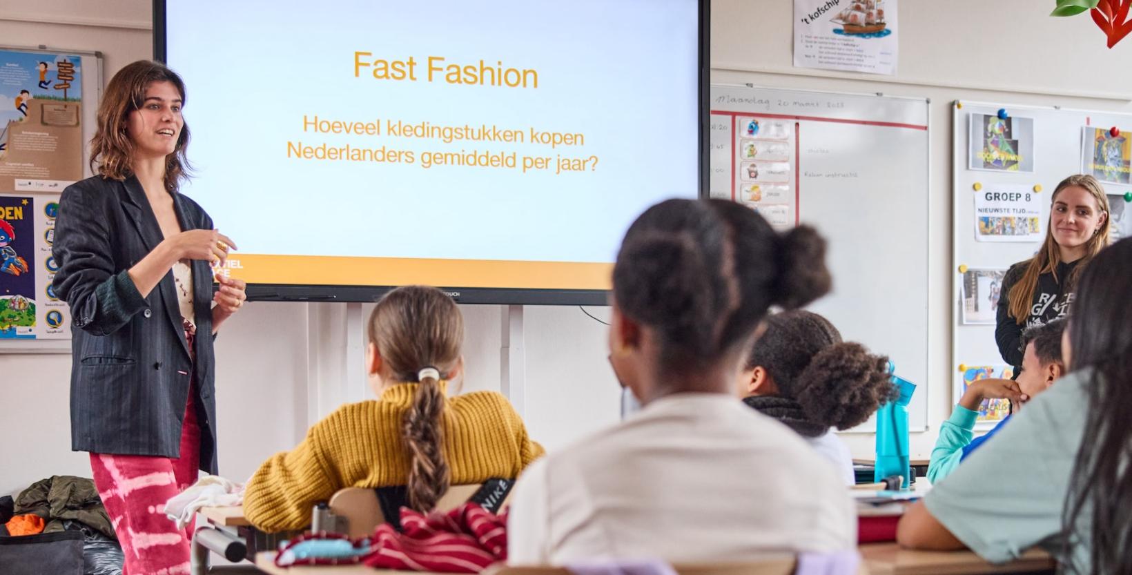 klimaatactivist en model Kiki Boreel staat voor  de klas te vertellen. Ze staat voor het digibord, met de tekst 'Fast Fashion'' 