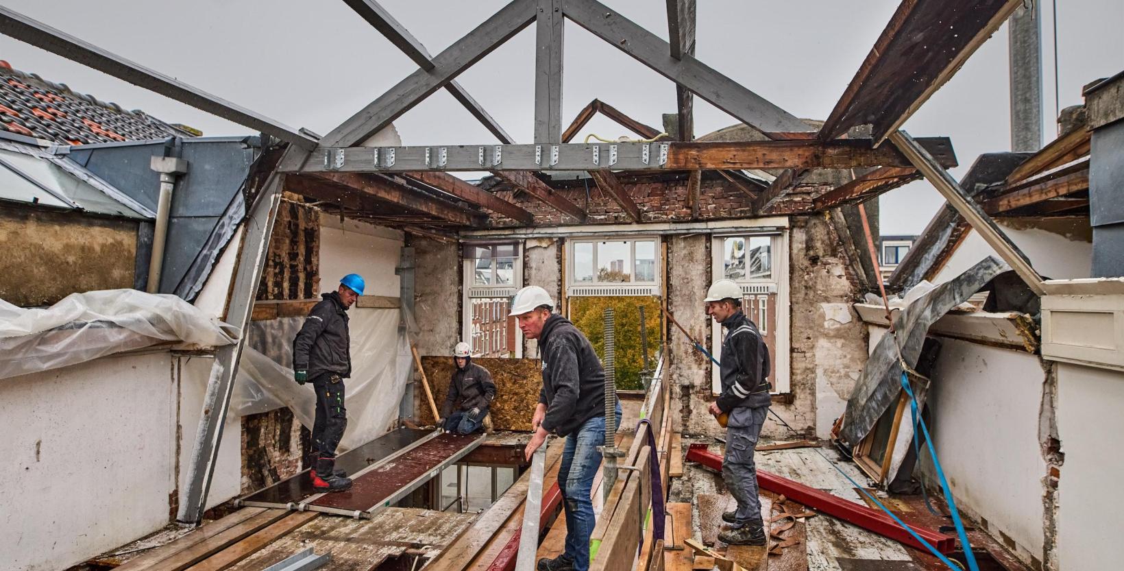 Vier bouwvakkers aan het werk met de sloop van de woningen aan de Claes de Vrieselaan. De bouwvakkers taan op de bovenste verdieping en het dak is verwijderd. 