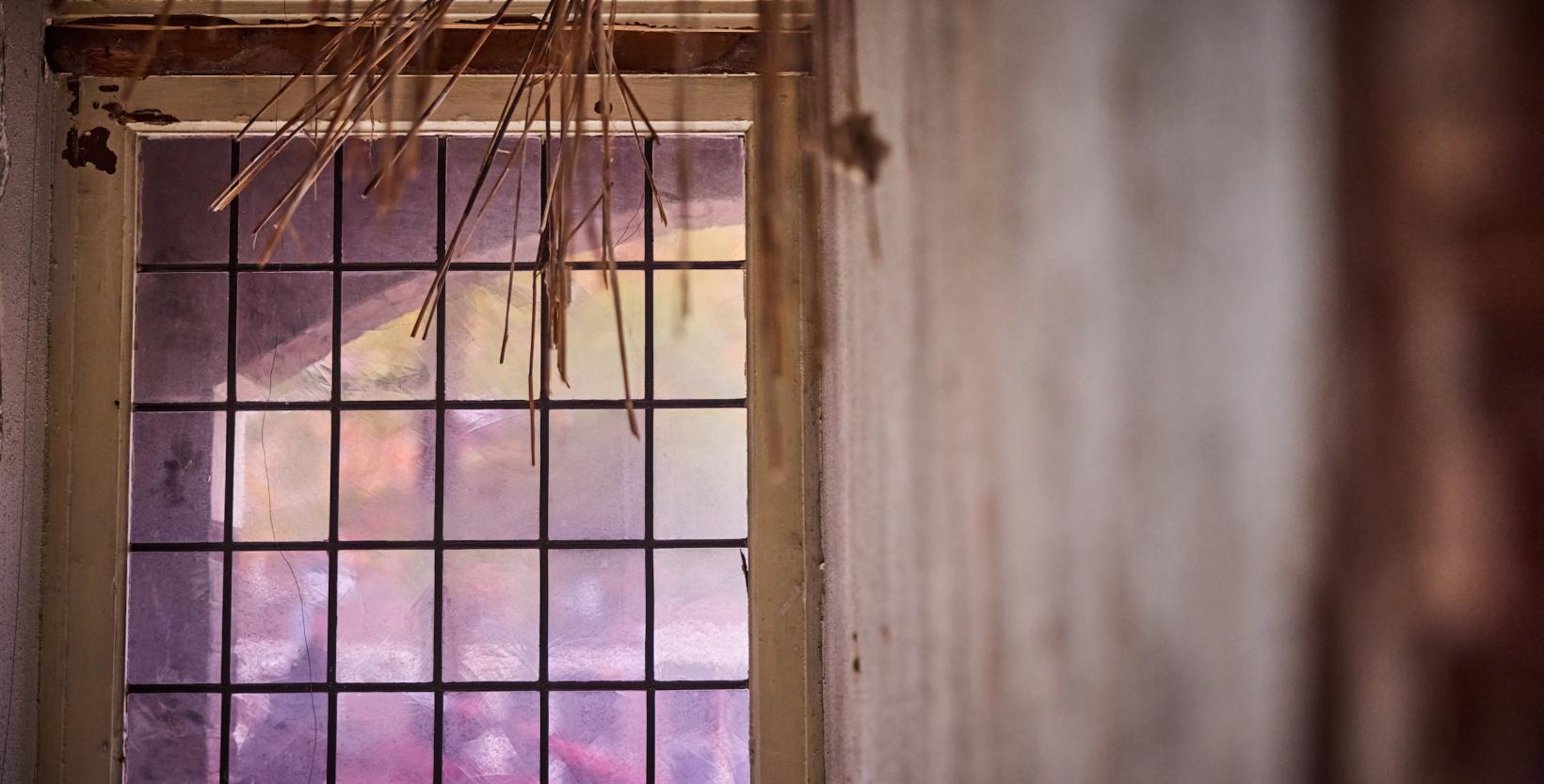 close-up van een glas in lood raam uit slooppand, stro komt uit het plafond 