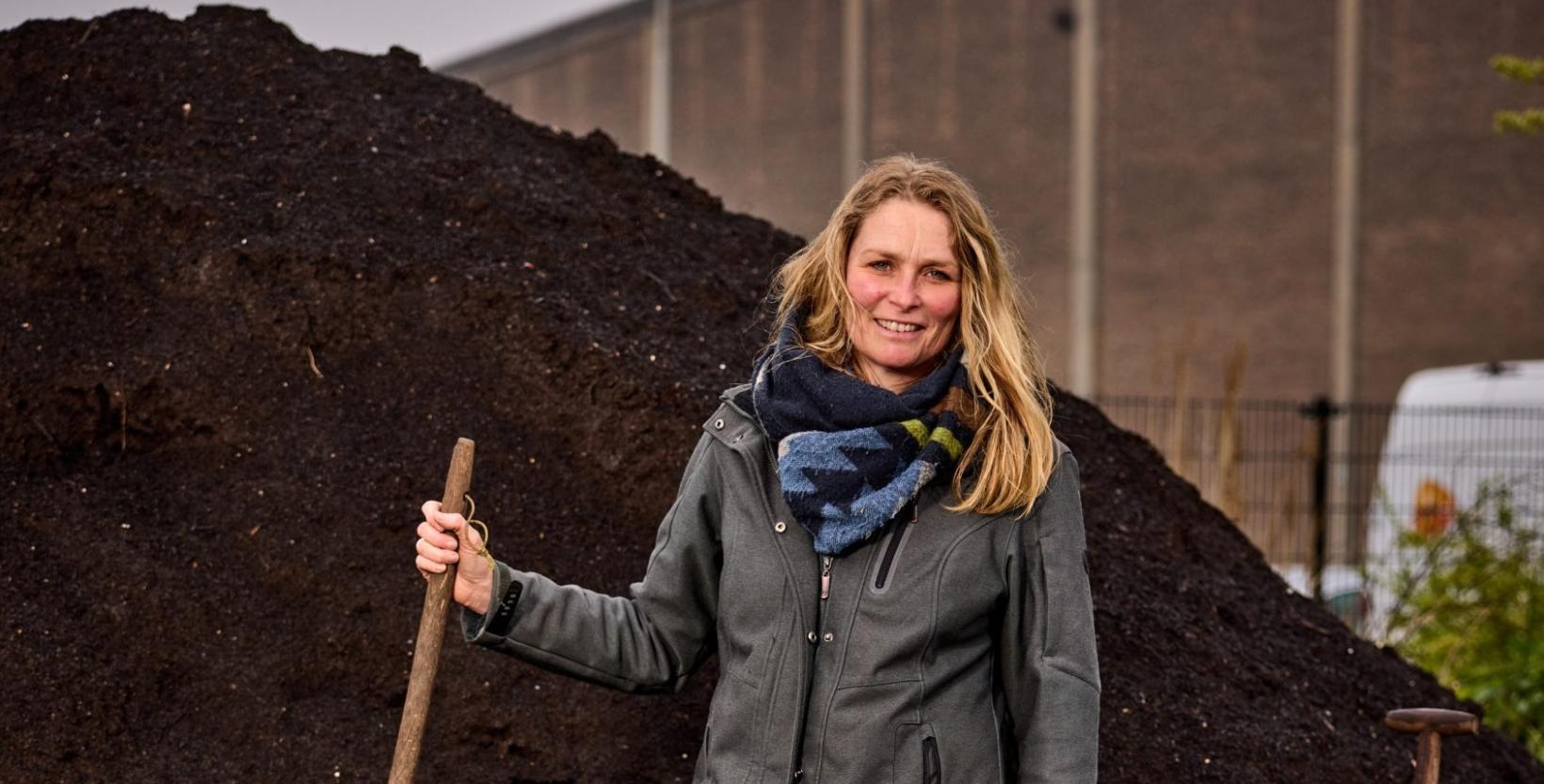 portret foto vrouw met schep in de hand voor een hoge composthoop