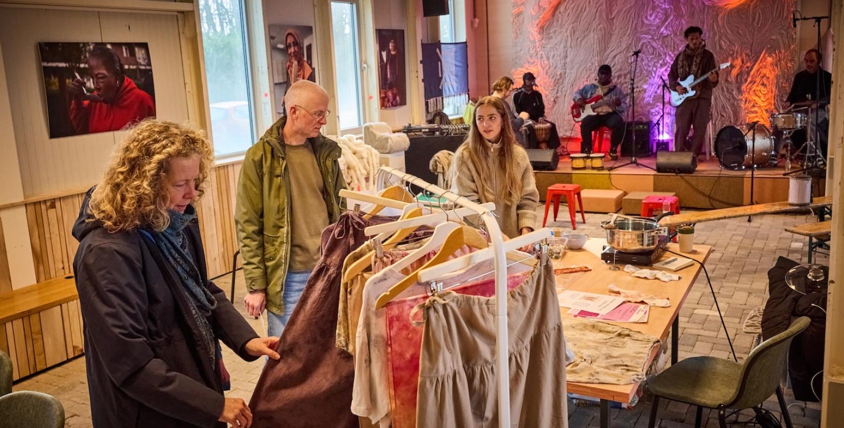 Bezoekers bekijken kleding terwijl op de achtergrond een band live muziek speelt tijdens een evenement.
