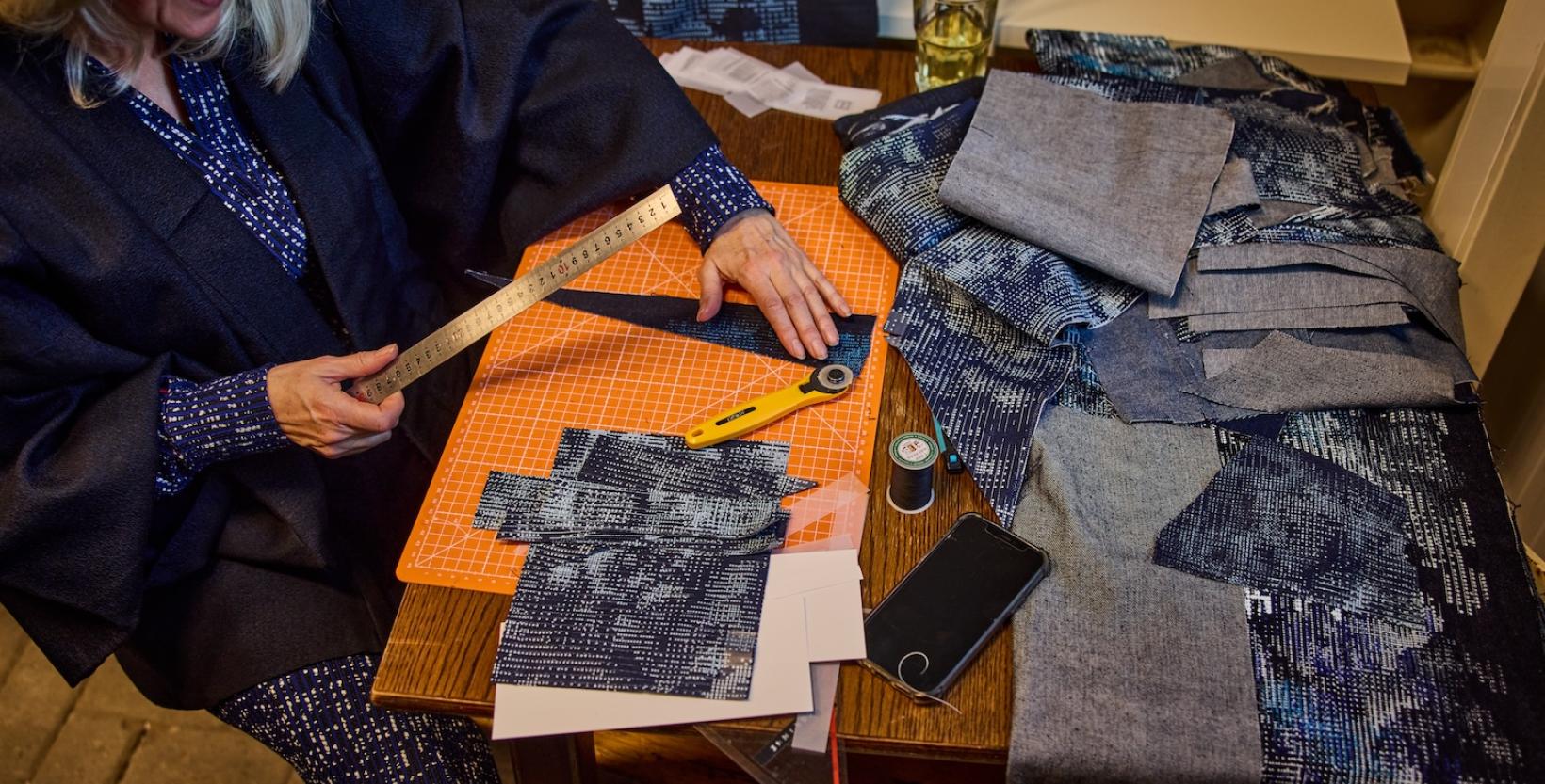 Maker snijdt en meet stukken stof op een werktafel tijdens een textielworkshop.