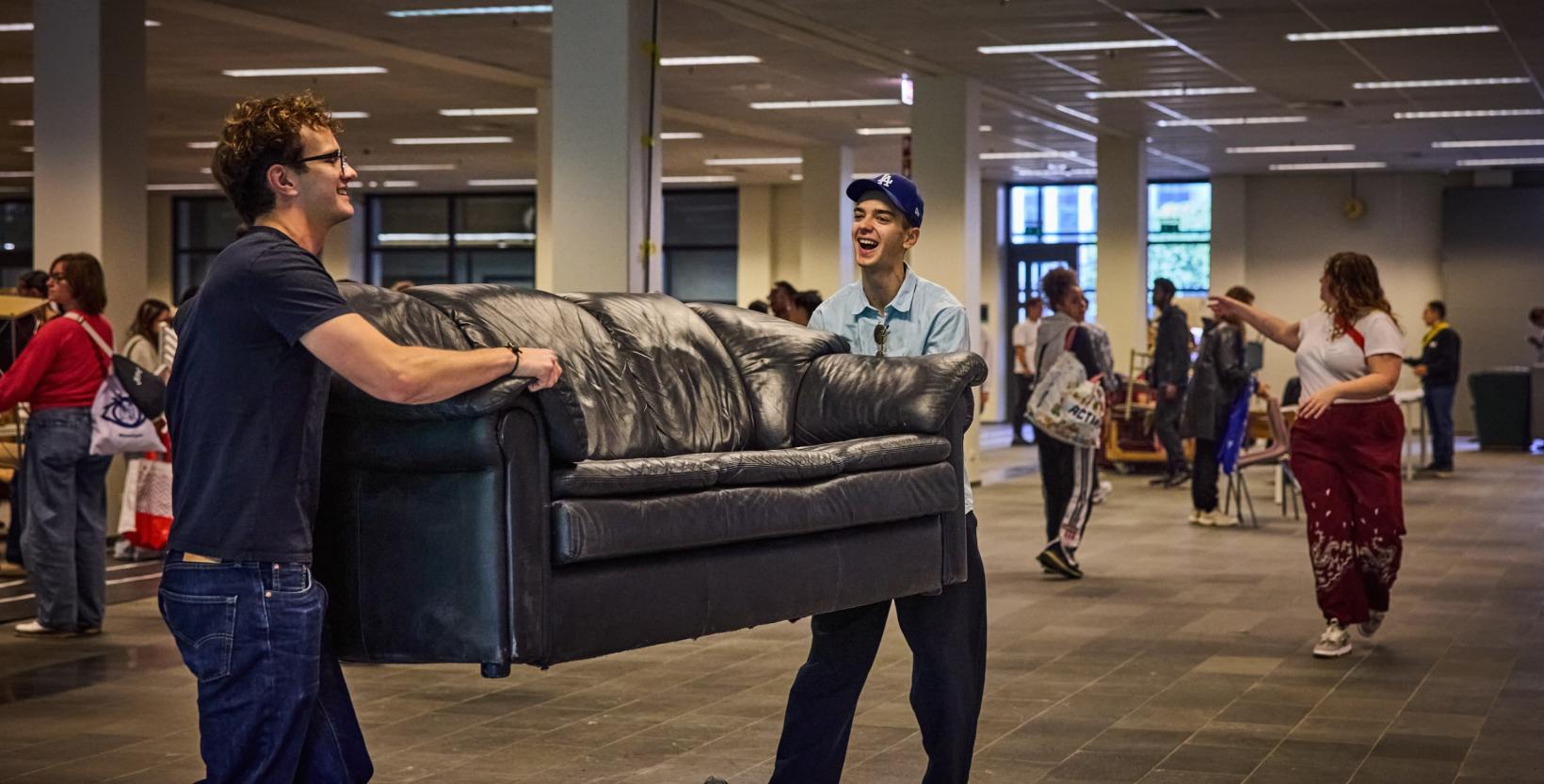 Studenten lopen rond tussen tweedehands meubels die zijn uitgestald in een grote hal.
