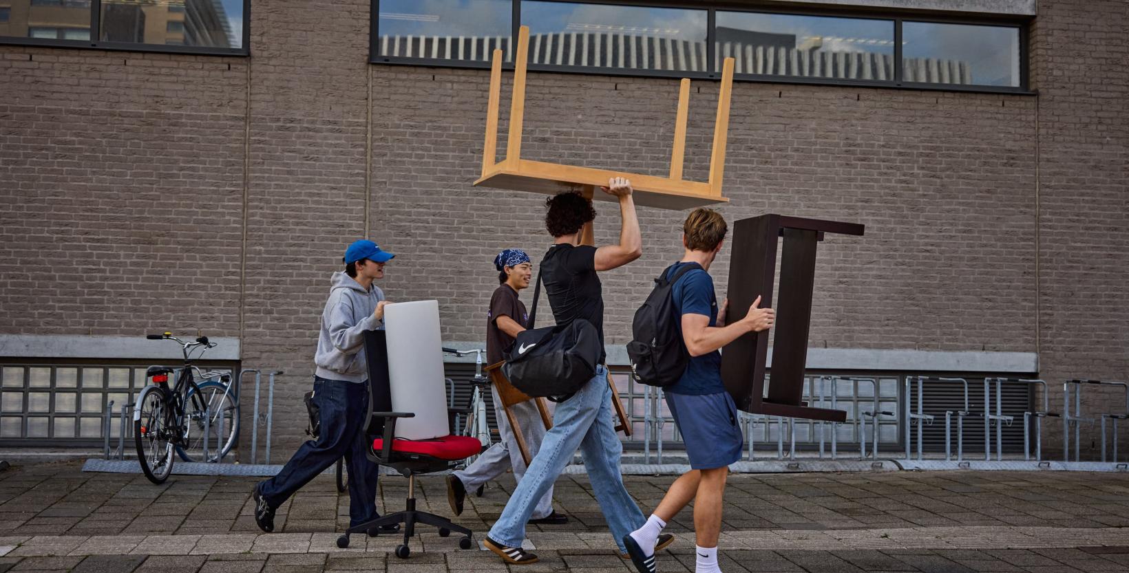 Studenten lopen rond tussen tweedehands meubels die zijn uitgestald in een grote hal.