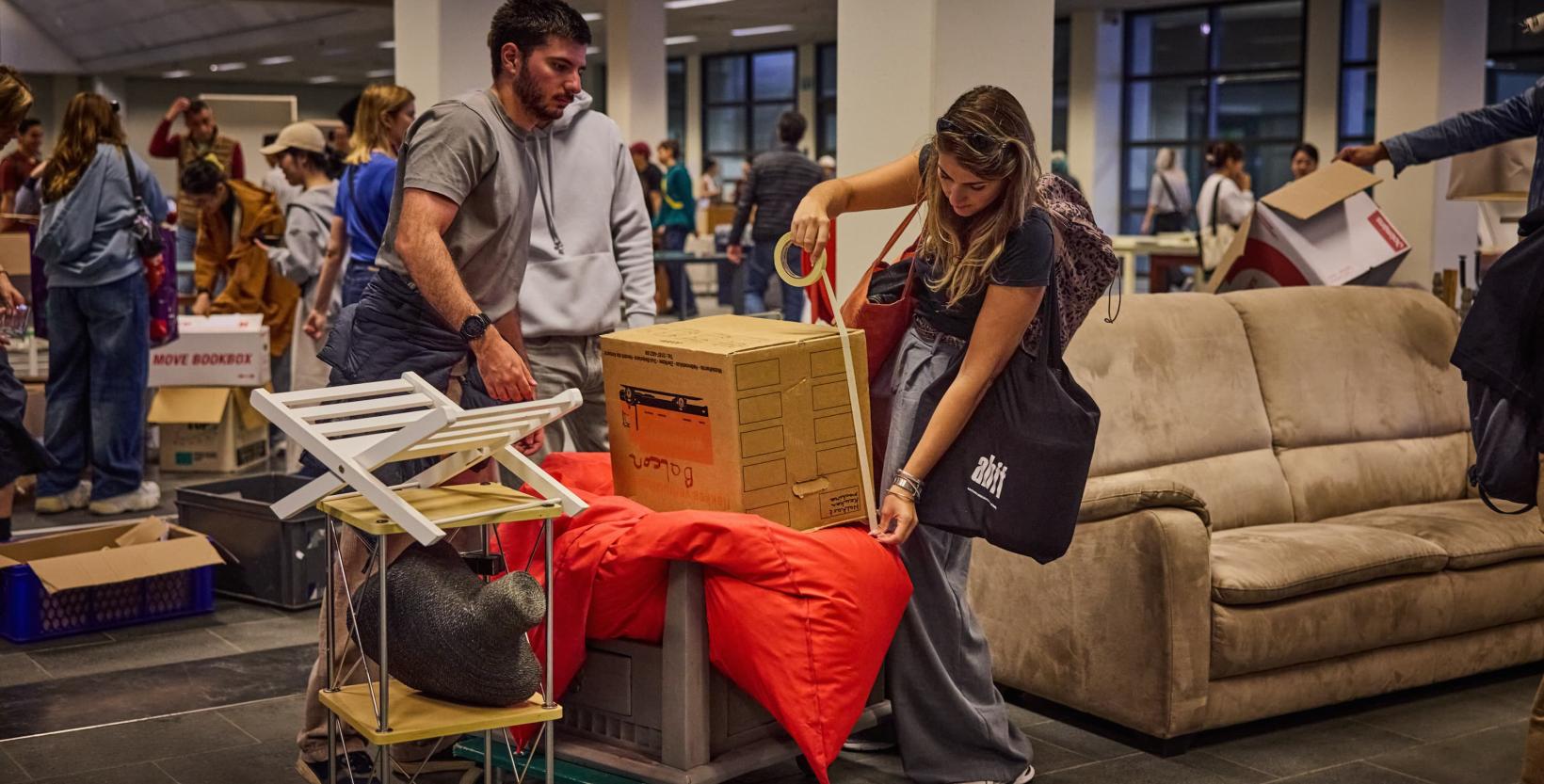 Studenten lopen rond tussen tweedehands meubels die zijn uitgestald in een grote hal.