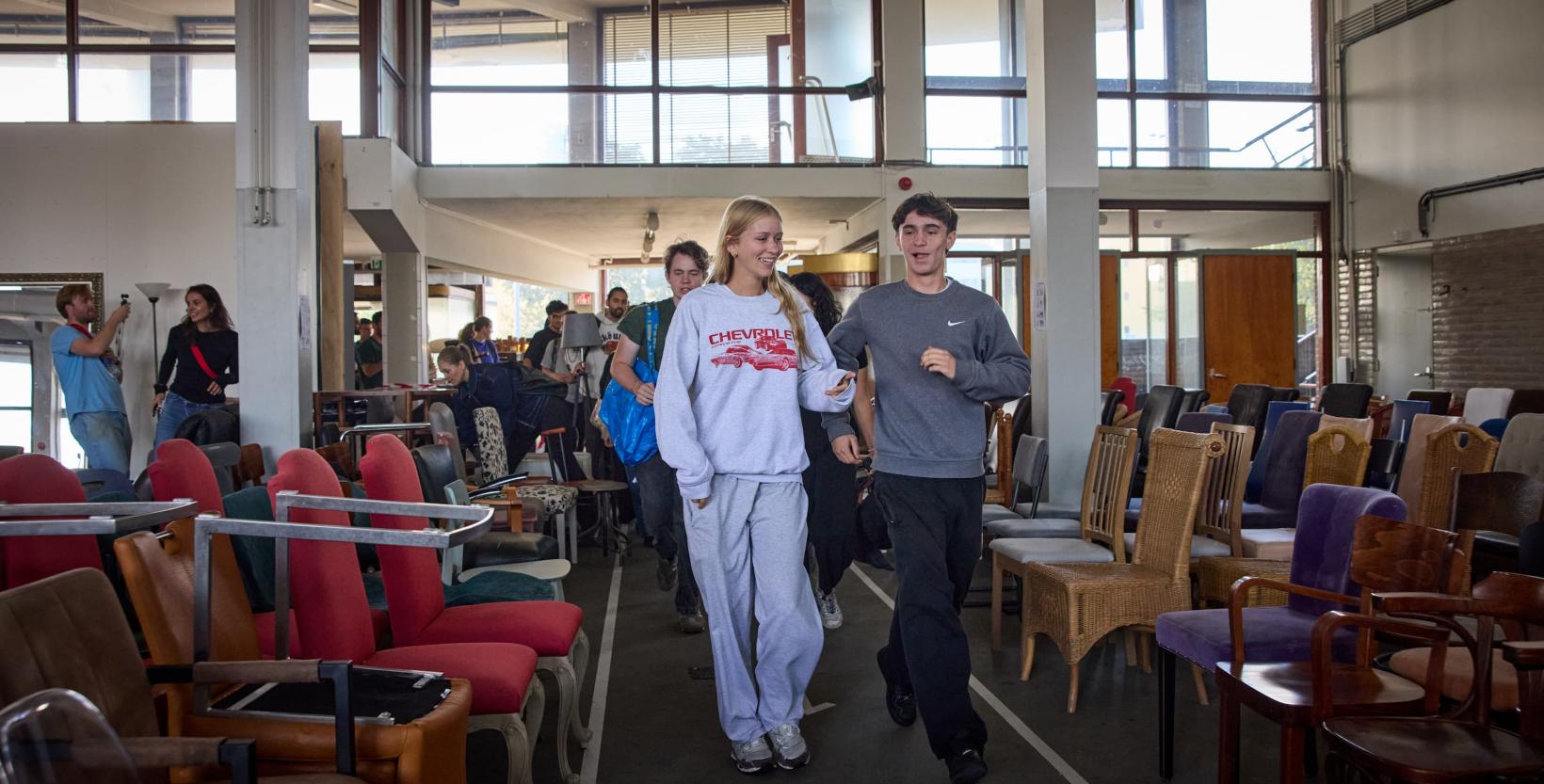 Studenten lopen rond tussen tweedehands meubels die zijn uitgestald in een grote hal.